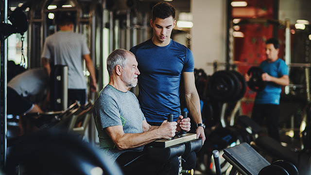 Fitnesstrainer trainiert älteren Mann 